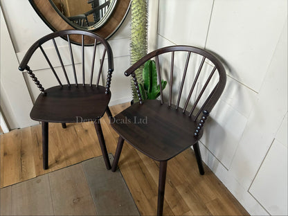 A wooden bobbin dining chair by Anthropologie placed at a rustic dining table, highlighting the carved spindle details and natural wood grain against a bright interior wall.
