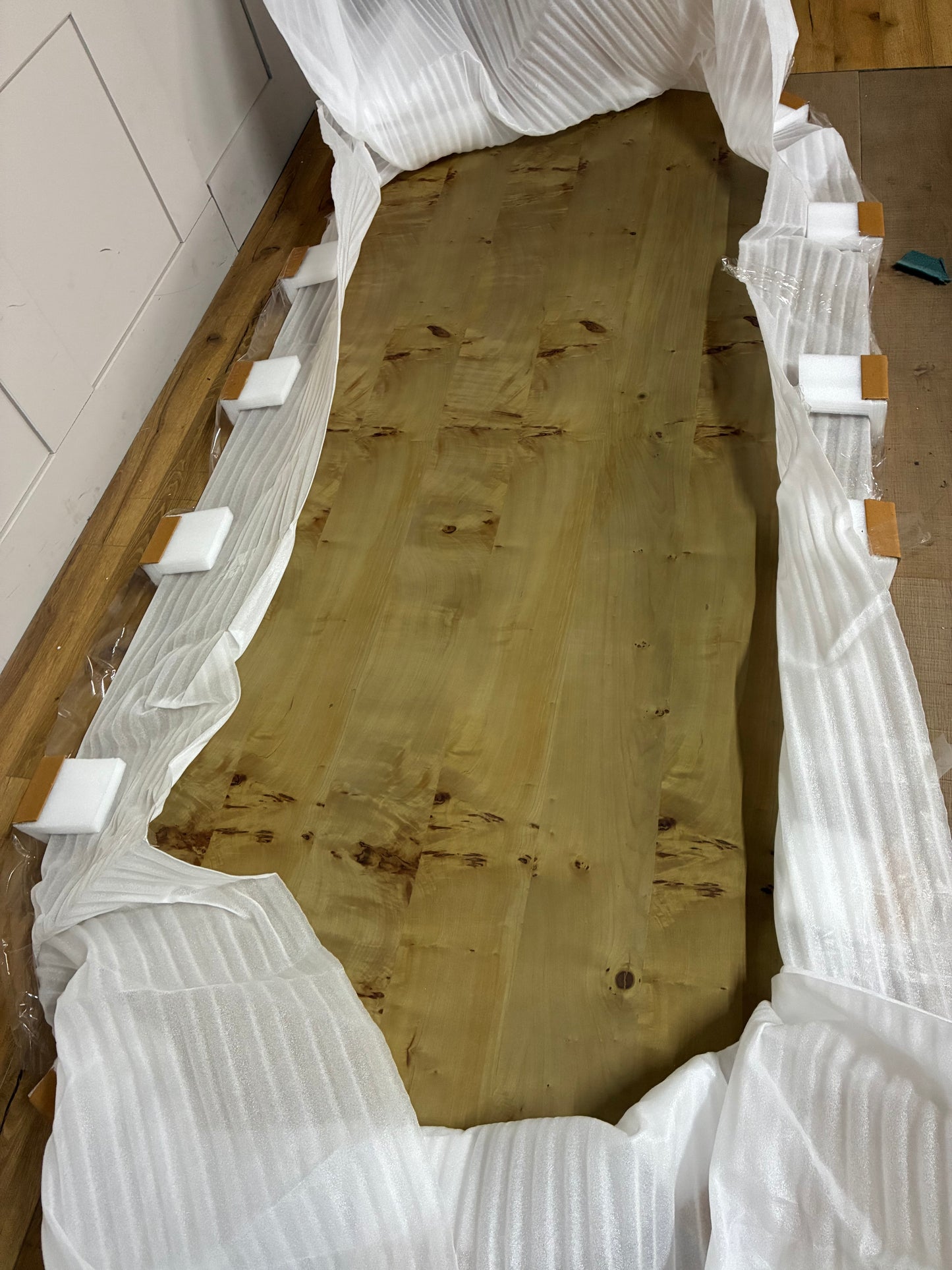 An Anthropologie Scout oval dining table made of light beige ash wood, featuring an oval tabletop with a decorative burl veneer pattern and thick, fluted pedestal legs. 