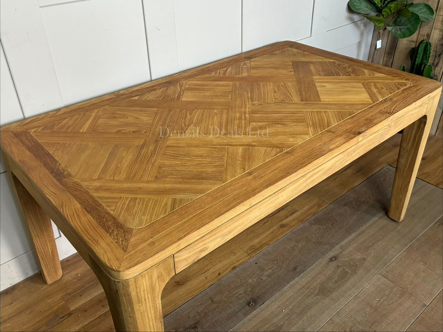 An eco-friendly rectangular dining table made of FSC-certified reclaimed solid teak. The tabletop showcases a light honey-toned, marquetry-inspired patchwork finish with natural wood grain variations, supported by clean-lined, solid wood legs."