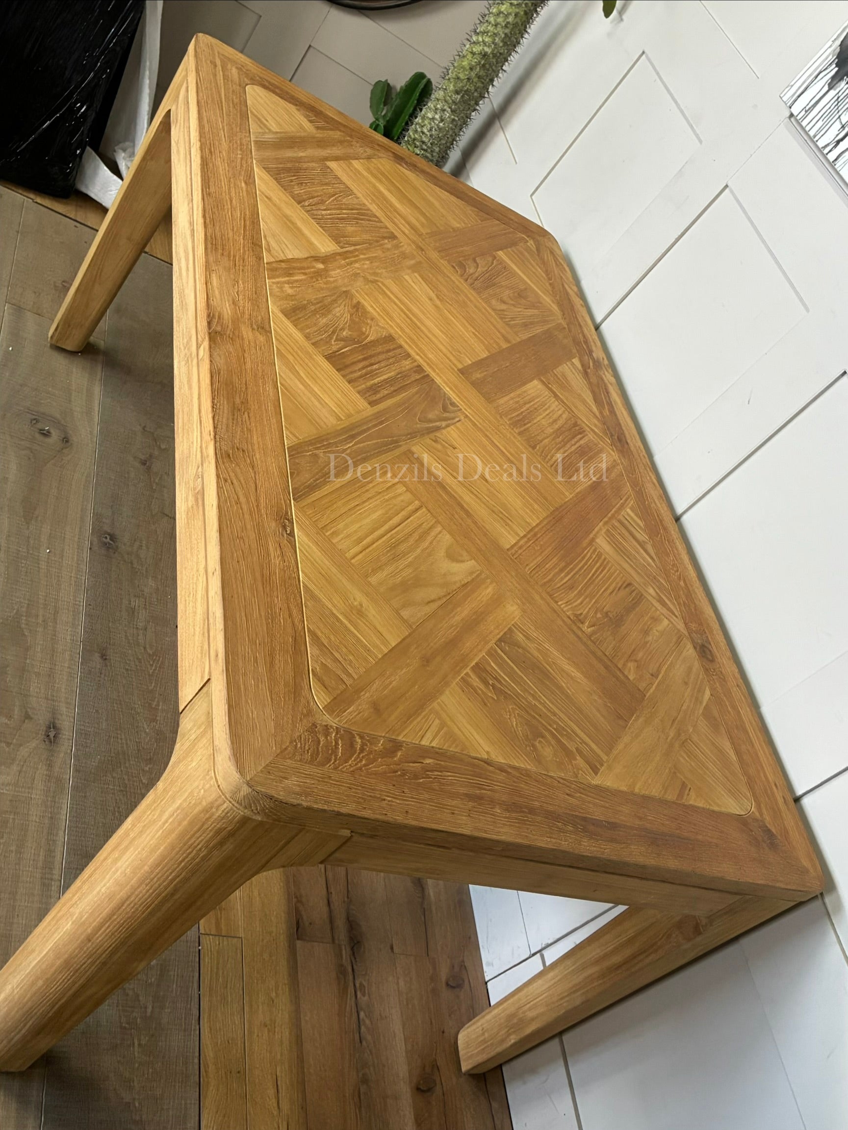 An eco-friendly rectangular dining table made of FSC-certified reclaimed solid teak. The tabletop showcases a light honey-toned, marquetry-inspired patchwork finish with natural wood grain variations, supported by clean-lined, solid wood legs."