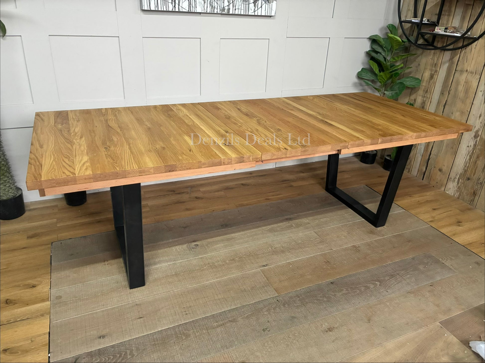 An industrial-style John Lewis Calia rectangular extending dining table. The table features a light-colored, wire-brushed solid oak top made of individual wood slats, supported by thick, angular black iron legs.