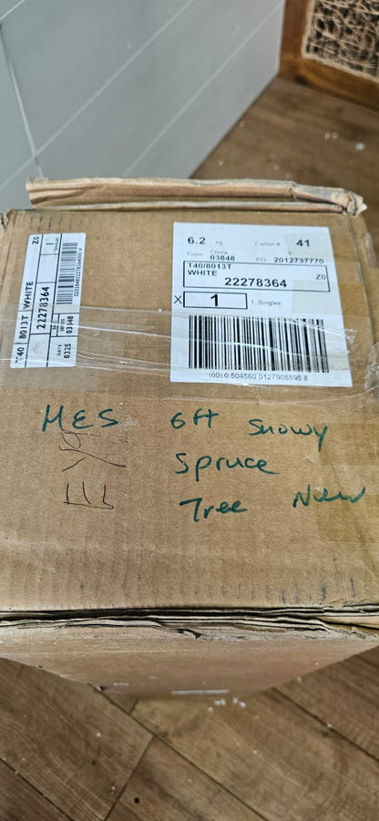 An unadorned M&S 6ft Snowy Spruce artificial Christmas tree with heavily snow-flocked white branches, standing elegantly in a festive living room setting.