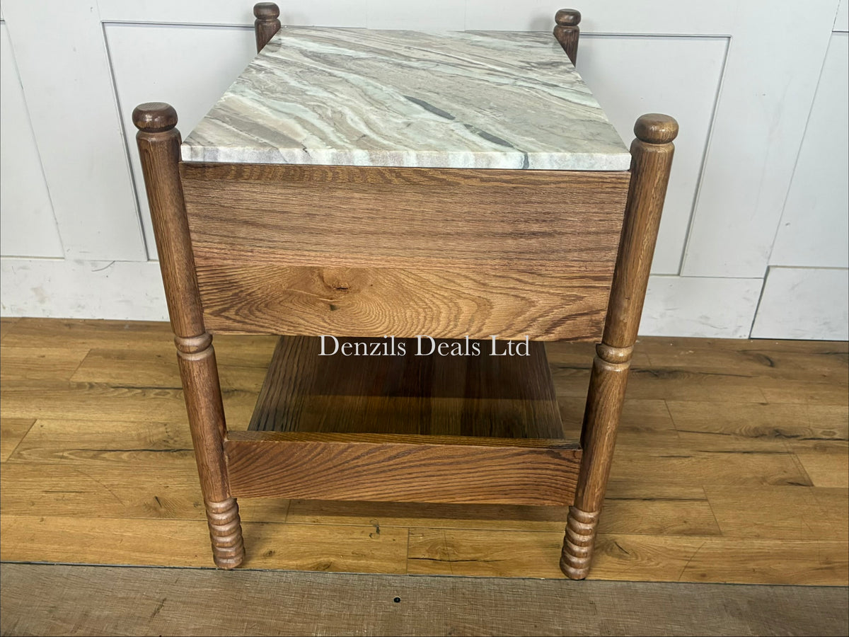 The Anthropologie Amelia Marble-Top Nightstand is a sophisticated bedside furniture piece that blends organic warmth with luxury materials. It features a premium Toronto marble top contrasted against an oak wood frame, complete with elegant spindled legs, a single storage drawer, and an open undermount shelf