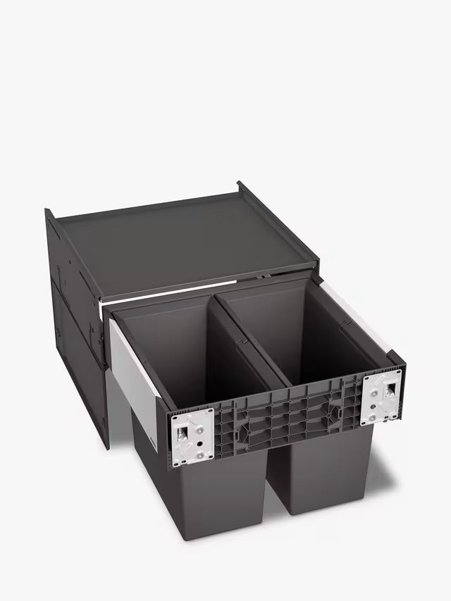 A BLANCO Select under-counter pull-out kitchen bin with two grey compartments, shown partially extended from a minimalist dark cabinet to reveal its 38-litre waste separation system. 