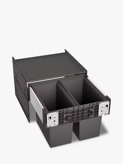 A BLANCO Select under-counter pull-out kitchen bin with two grey compartments, shown partially extended from a minimalist dark cabinet to reveal its 38-litre waste separation system. 