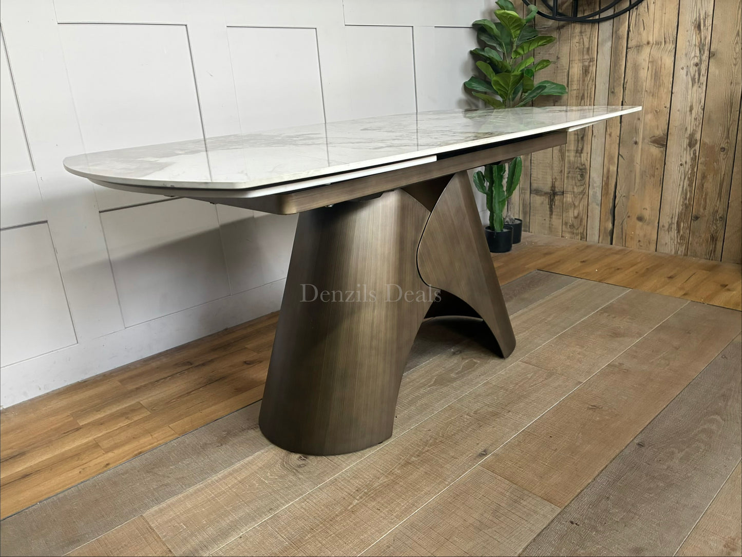 by a heavy-duty, sculptural metal pedestal base finished in a warm, matte bronze tone. The tabletop features a clean, seamless look with hidden internal tracking lines, illustrating its rotating extension mechanism that smoothly expands the surface from a compact six-seater to a larger eight-seater.