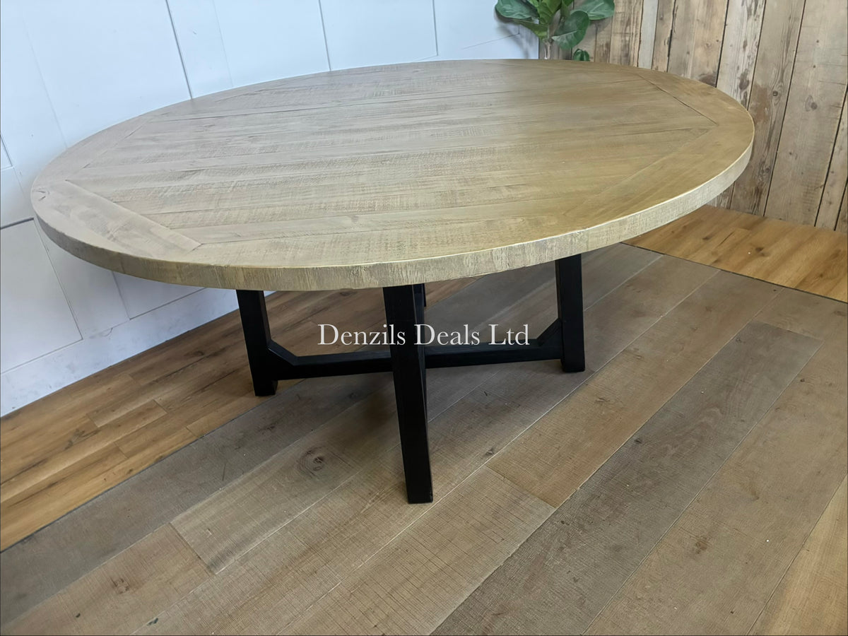 Cox & Cox Belluno round dining table with a 160cm diameter top made of natural pine wood, supported by striking black legs that intersect in a central cross design
