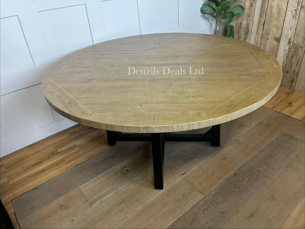 Cox & Cox Belluno round dining table with a 160cm diameter top made of natural pine wood, supported by striking black legs that intersect in a central cross design