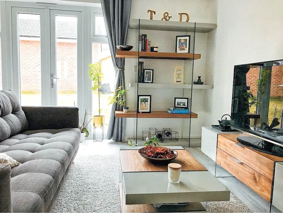 Dwell Sturado shelving unit styled in a modern living room, loaded with decorative vases, hardcover books, and potted plants."