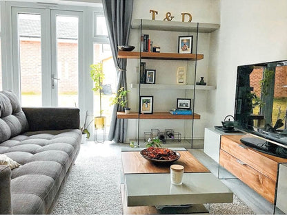 Dwell Sturado shelving unit styled in a modern living room, loaded with decorative vases, hardcover books, and potted plants."