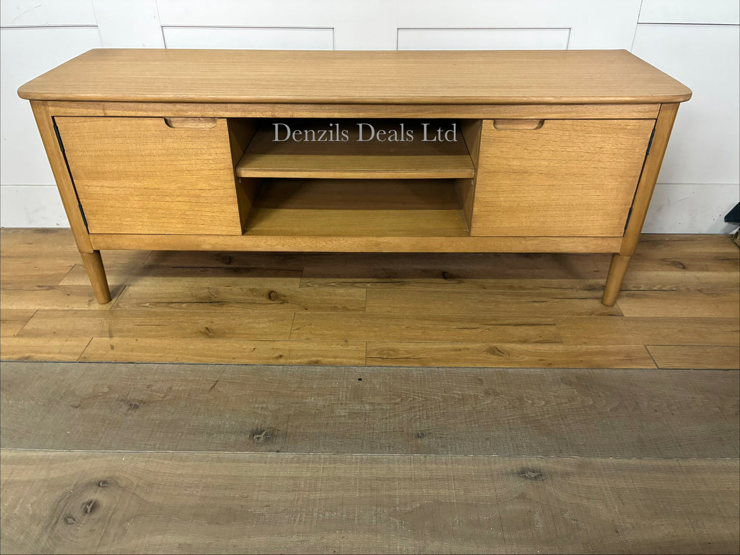 Fishe and Lilly Norway Oak TV Stand and Media Unit made of solid white cedar wood. The mid-century Scandinavian design features a warm oak finish, an open center shelving section for media devices, and integrated storage doors on the sides, supported by angled wooden legs."