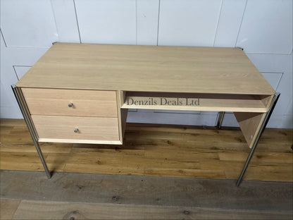 Front view of the John Lewis Hansen 2-drawer desk in a natural light oak finish. The desk has a minimalist, contemporary design with a smooth rectangular tabletop. Directly beneath the surface are two wide drawers sitting flush against the frame, separated by a slim central partition. Below the drawers is a full-width open storage shelf. The entire unit is supported by four slender, square legs crafted from matching solid oak wood.
