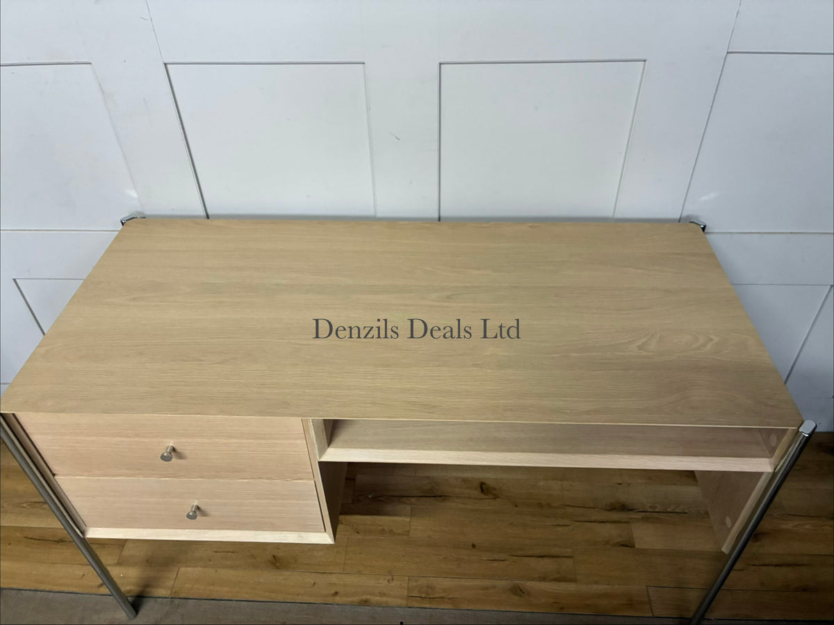 Front view of the John Lewis Hansen 2-drawer desk in a natural light oak finish. The desk has a minimalist, contemporary design with a smooth rectangular tabletop. Directly beneath the surface are two wide drawers sitting flush against the frame, separated by a slim central partition. Below the drawers is a full-width open storage shelf. The entire unit is supported by four slender, square legs crafted from matching solid oak wood.