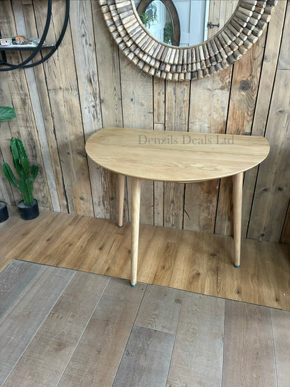 Gallery Direct Lewes oak dining table shown with its side leaves folded down vertically for compact, space-saving storage against a wall.