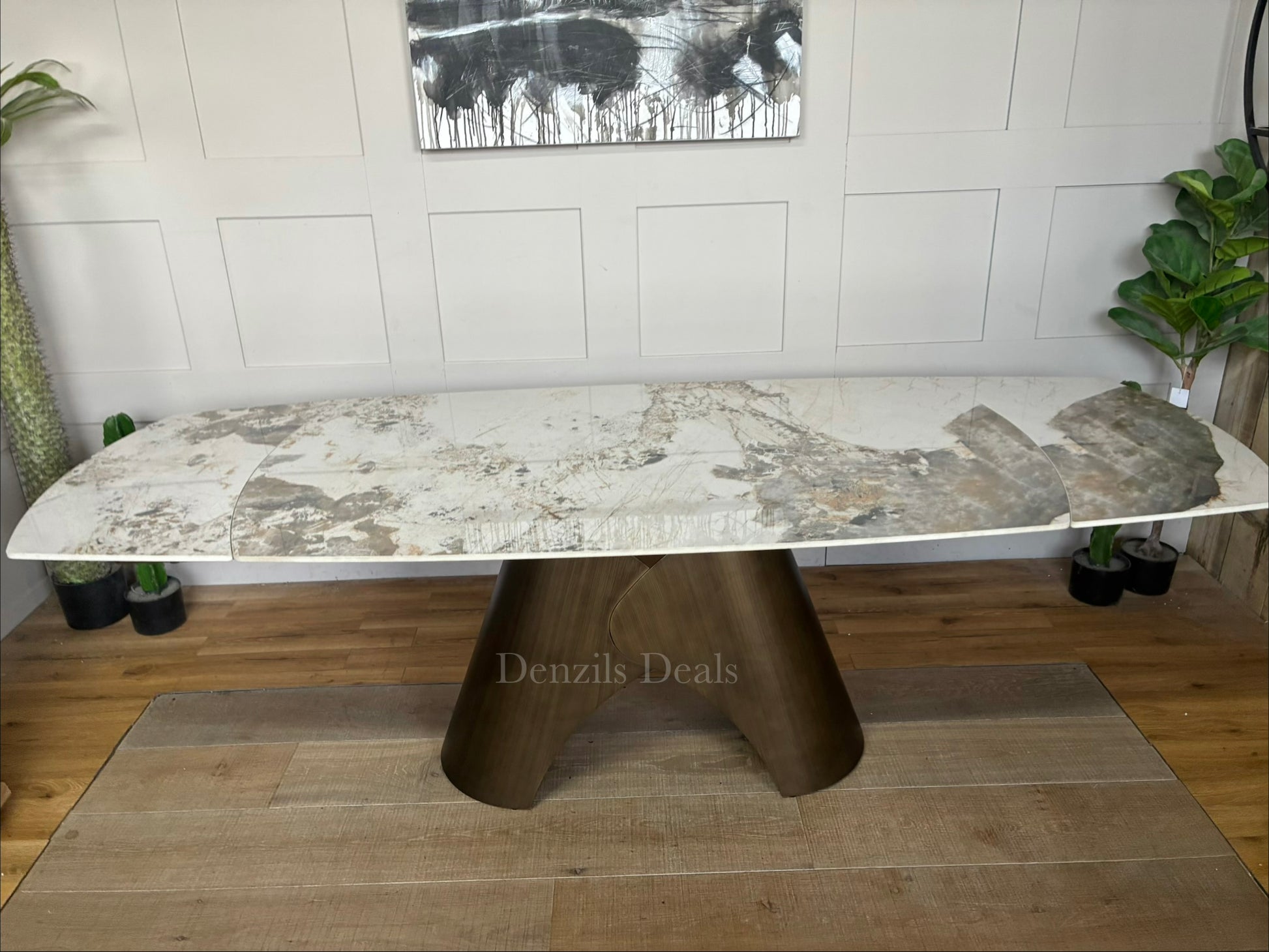 by a heavy-duty, sculptural metal pedestal base finished in a warm, matte bronze tone. The tabletop features a clean, seamless look with hidden internal tracking lines, illustrating its rotating extension mechanism that smoothly expands the surface from a compact six-seater to a larger eight-seater.