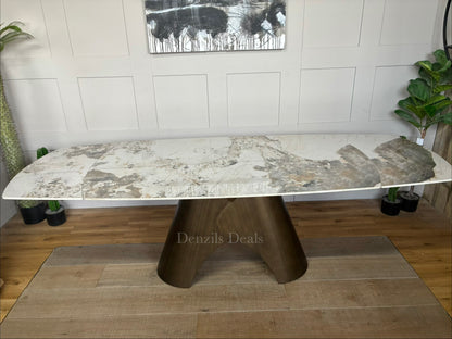 by a heavy-duty, sculptural metal pedestal base finished in a warm, matte bronze tone. The tabletop features a clean, seamless look with hidden internal tracking lines, illustrating its rotating extension mechanism that smoothly expands the surface from a compact six-seater to a larger eight-seater.