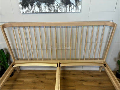 A super king-size bed frame made from natural-toned solid ash wood. The headboard has a distinctive curved silhouette with elegant turned spindles. The frame features softened profiles and fine veneers, supported by tapered wooden legs with 21.5cm of floor clearance