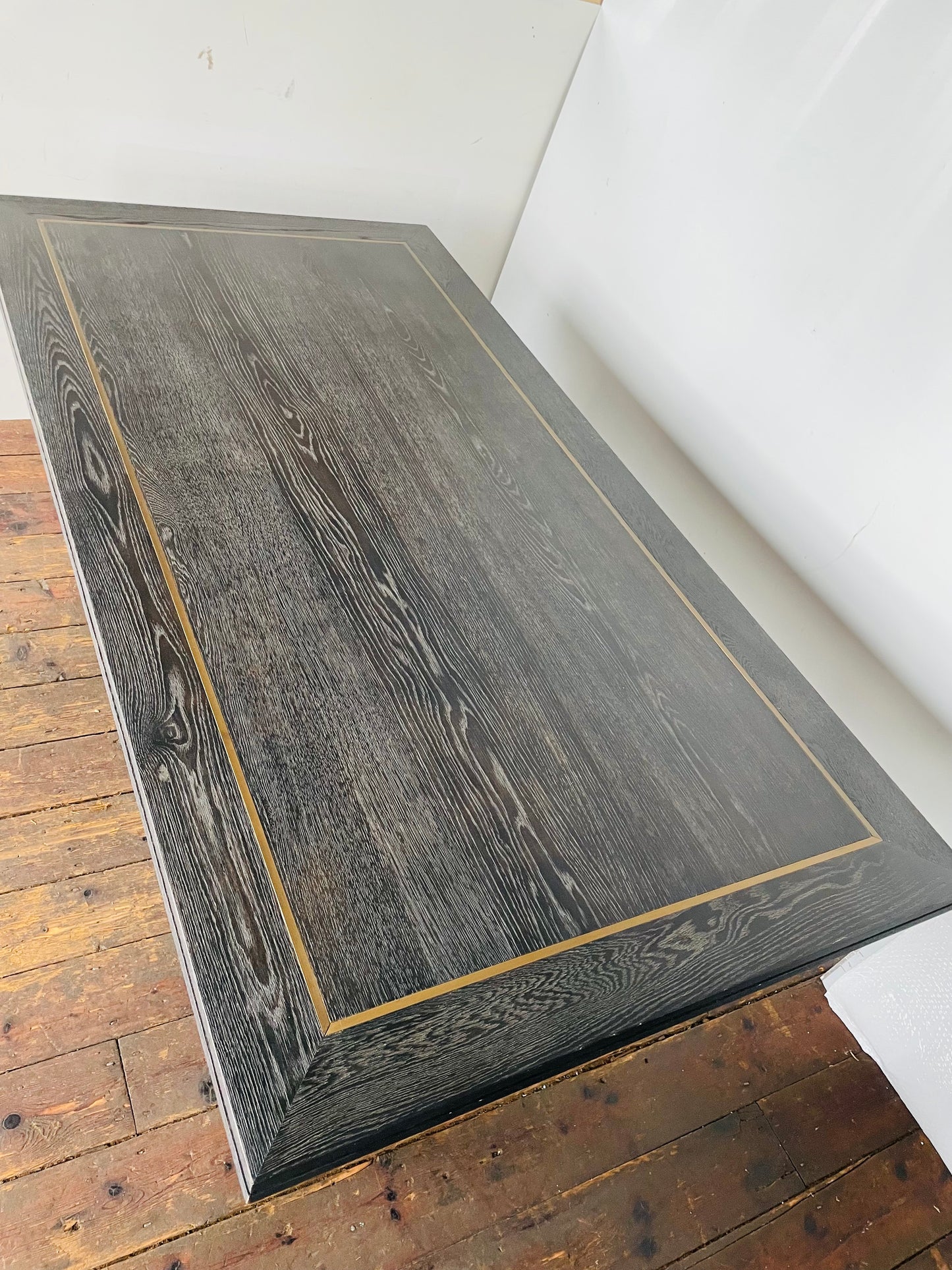 A small rectangular Richmond Interiors Hunter dining table featuring a black oak veneer tabletop with matte brushed gold metal legs and geometric corner inlay details. 