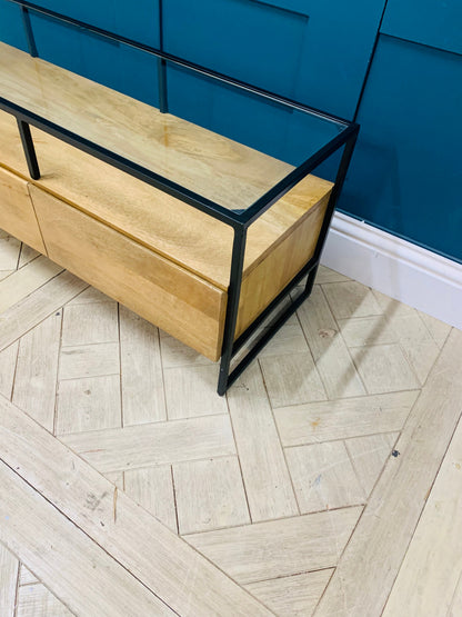 Industrial-style Made.com Kilby Wide TV stand. Features a warm, light mango wood grain base with two roomy storage drawers on clean, black metal legs. The top of the unit is a sleek smoked black glass, designed for placing a media console or television