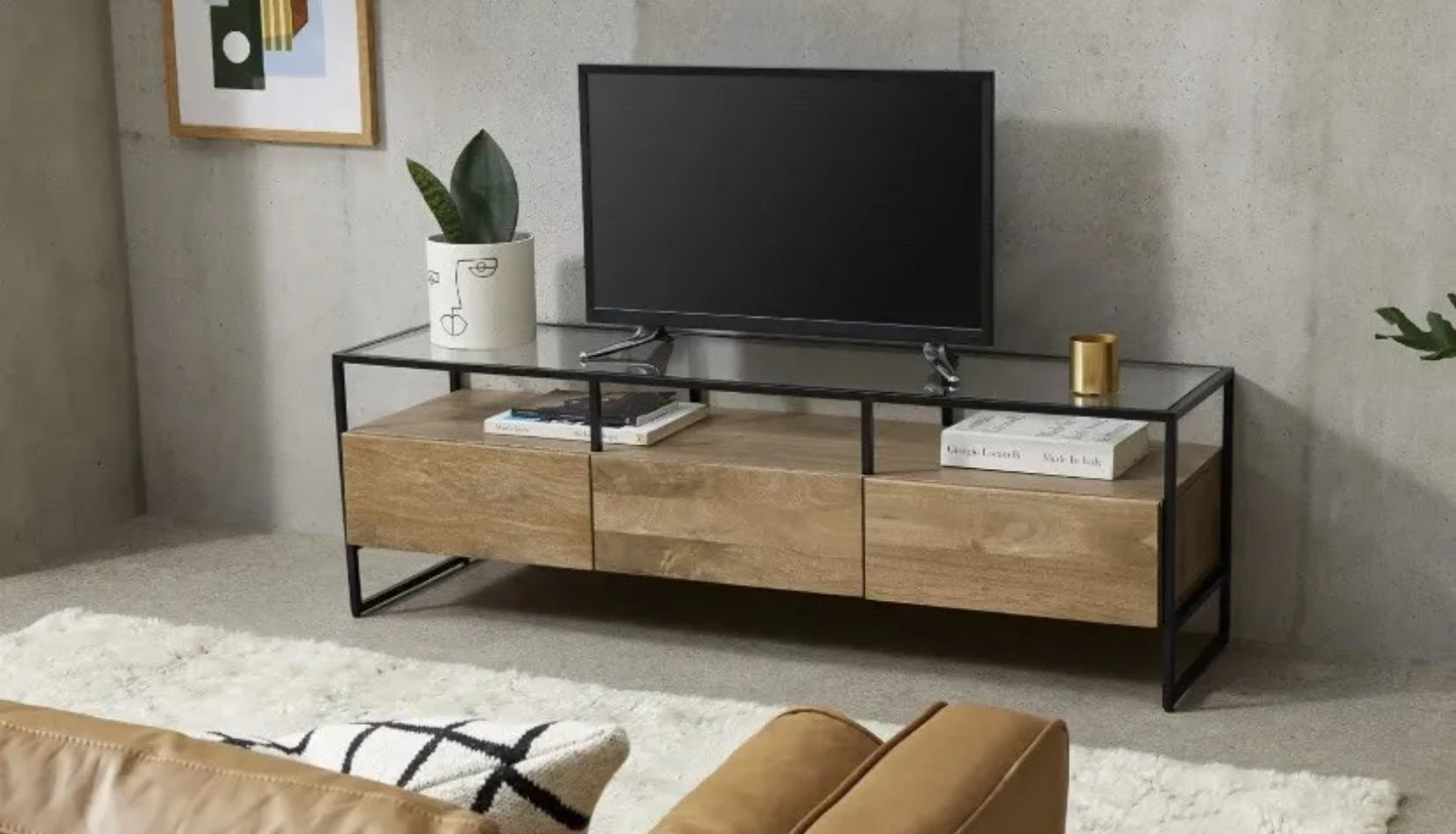 Industrial-style Made.com Kilby Wide TV stand. Features a warm, light mango wood grain base with two roomy storage drawers on clean, black metal legs. The top of the unit is a sleek smoked black glass, designed for placing a media console or television