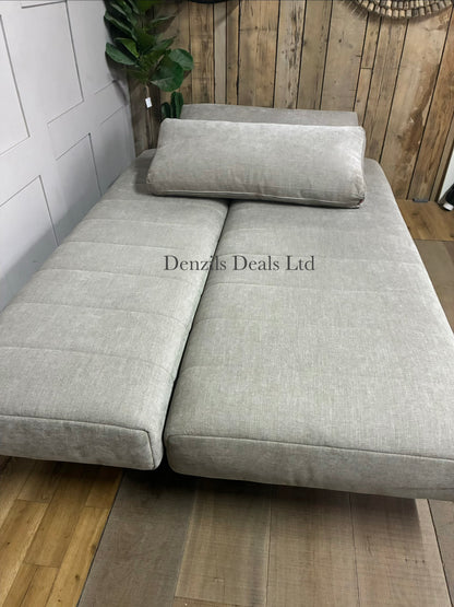 A minimalist Innovation Living Ripple two-seater sofa bed upholstered in smooth, neutral Avella Sand 280 fabric. The sofa features a clean, subdued modern design with tight cushioning, sleek wooden legs, and a sturdy metal frame.