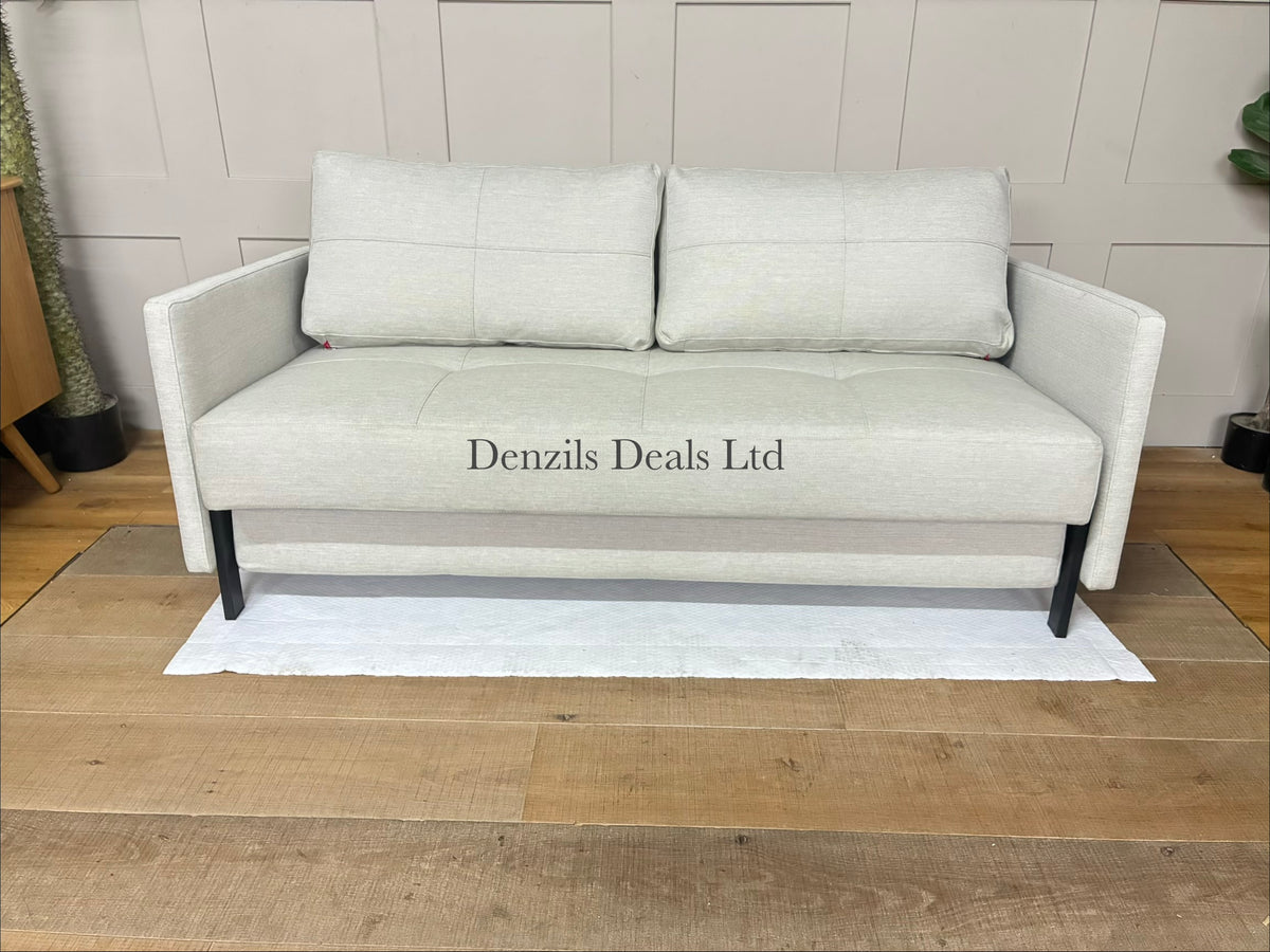 Scandinavian-style sofa bed in textured beige fabric with oak legs, shown as a cozy, compact living room seat.