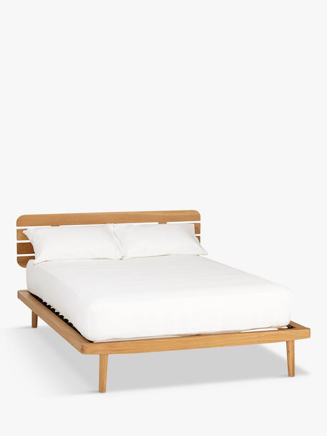 A modern bedroom setup featuring the John Lewis Bow king-size oak bed frame with an upholstered headboard, styled with neutral bedding