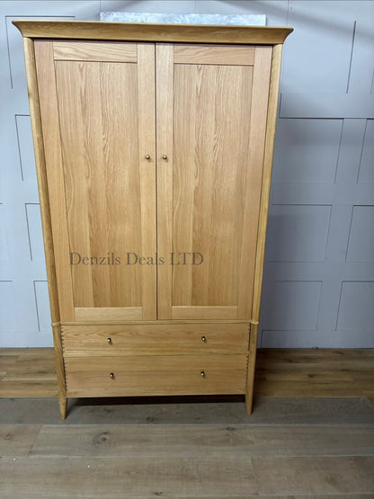 John Lewis Essence Double Wardrobe, Oak. This modern wardrobe showcases the natural grain and warm tones of oak wood. It features two full-length flush doors with clean vertical cutouts serving as minimalist handles, resting on a subtle, matching wooden base.