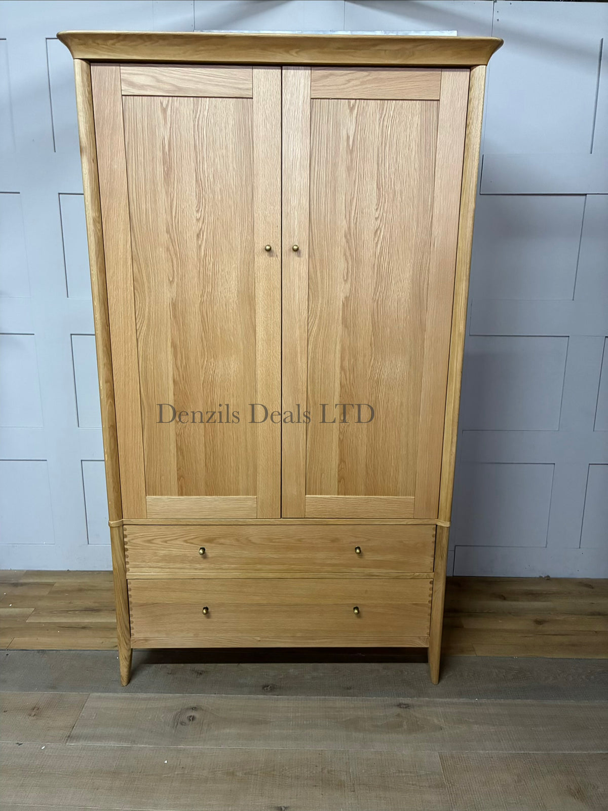John Lewis Essence Double Wardrobe, Oak. This modern wardrobe showcases the natural grain and warm tones of oak wood. It features two full-length flush doors with clean vertical cutouts serving as minimalist handles, resting on a subtle, matching wooden base.