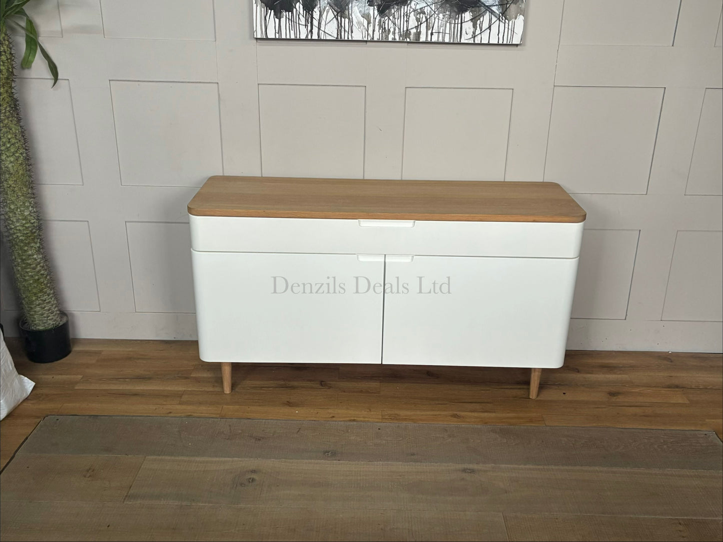 John Lewis Mira wide Scandinavian-style sideboard featuring a white painted frame and cabinet doors, a natural solid oak top, a wide divided top drawer with integrated handles, smooth rounded corners, and sleek tapered wooden legs.