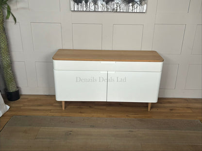 John Lewis Mira wide Scandinavian-style sideboard featuring a white painted frame and cabinet doors, a natural solid oak top, a wide divided top drawer with integrated handles, smooth rounded corners, and sleek tapered wooden legs.