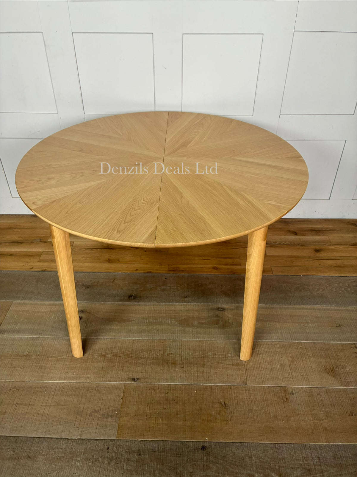 A contemporary John Lewis Notch round dining table made from natural oak, featuring a distinctive starburst veneer pattern on its circular top and sturdy, clean-lined legs. The table expands from a 4-seater to a 6-seater using a central fold-out extension leaf."