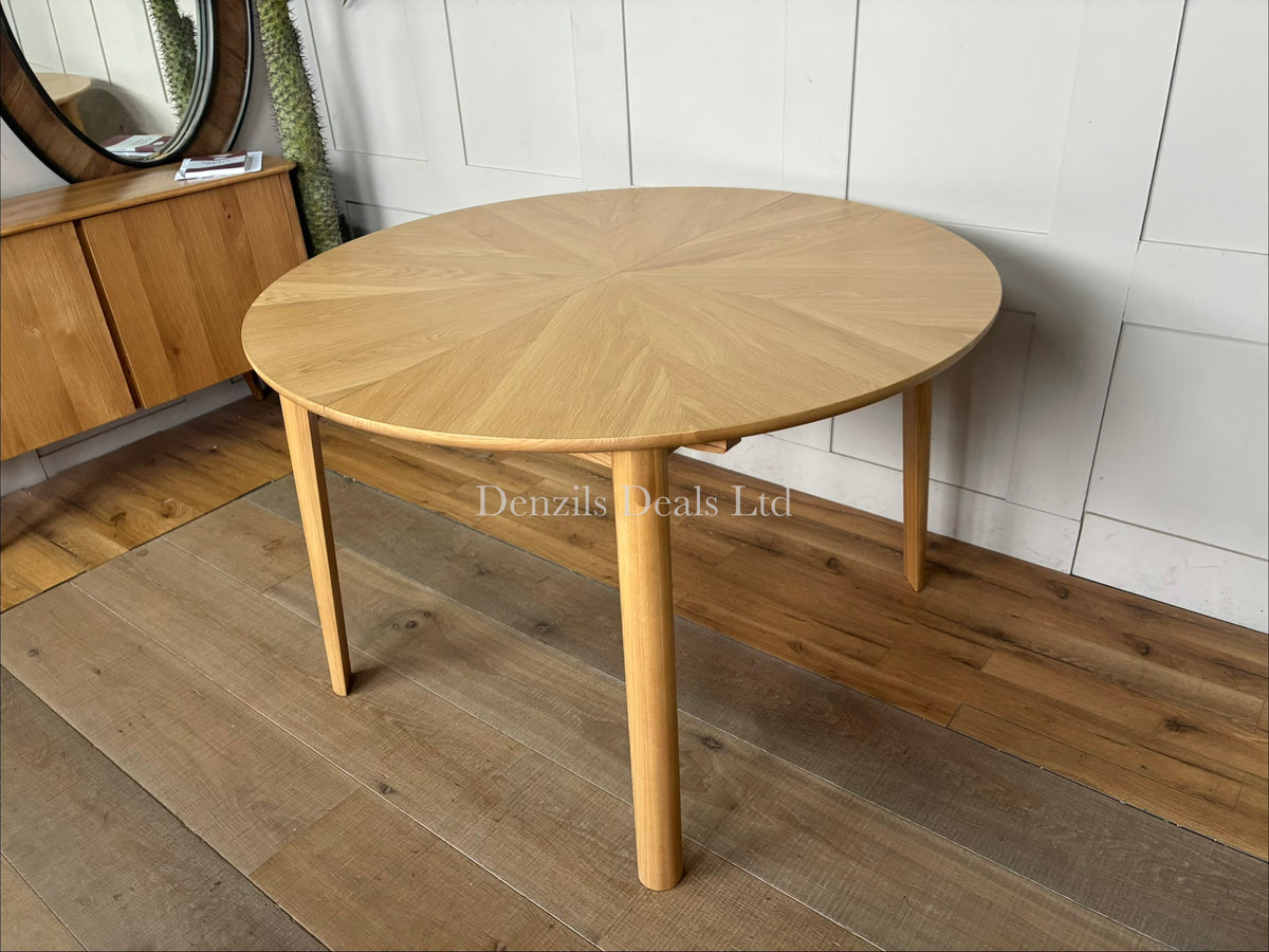 A contemporary John Lewis Notch round dining table made from natural oak, featuring a distinctive starburst veneer pattern on its circular top and sturdy, clean-lined legs. The table expands from a 4-seater to a 6-seater using a central fold-out extension leaf."