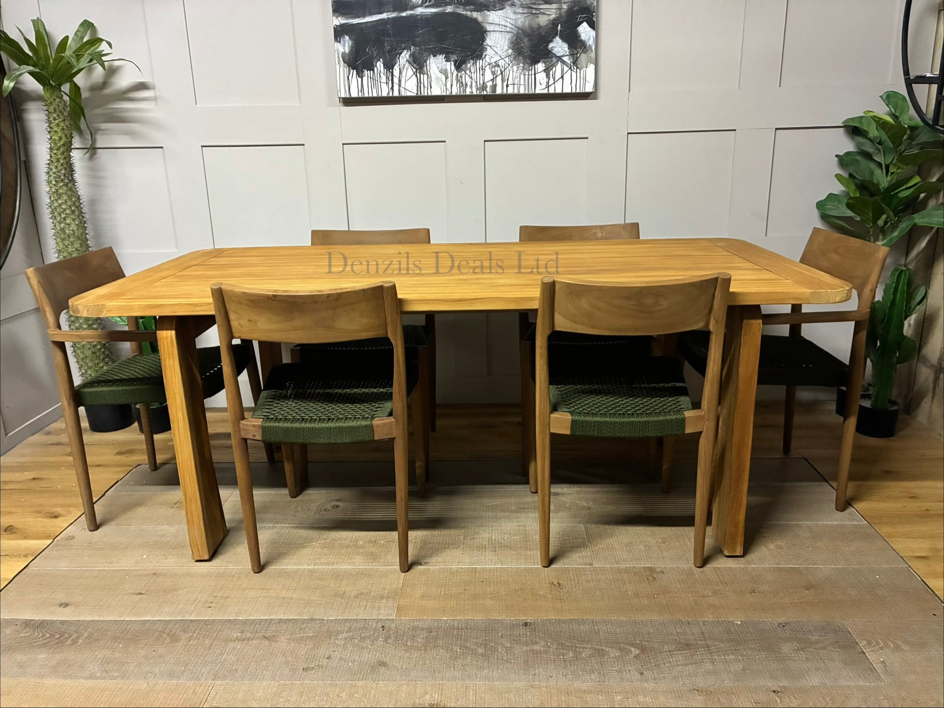Outdoor dining set featuring a contemporary rectangular table and six matching Scandi-style dining chairs, arranged on a sunny patio. The natural teak wood furniture features smooth, rounded corners and modern, blocky, upholstered seating with shower-resistant cushions."