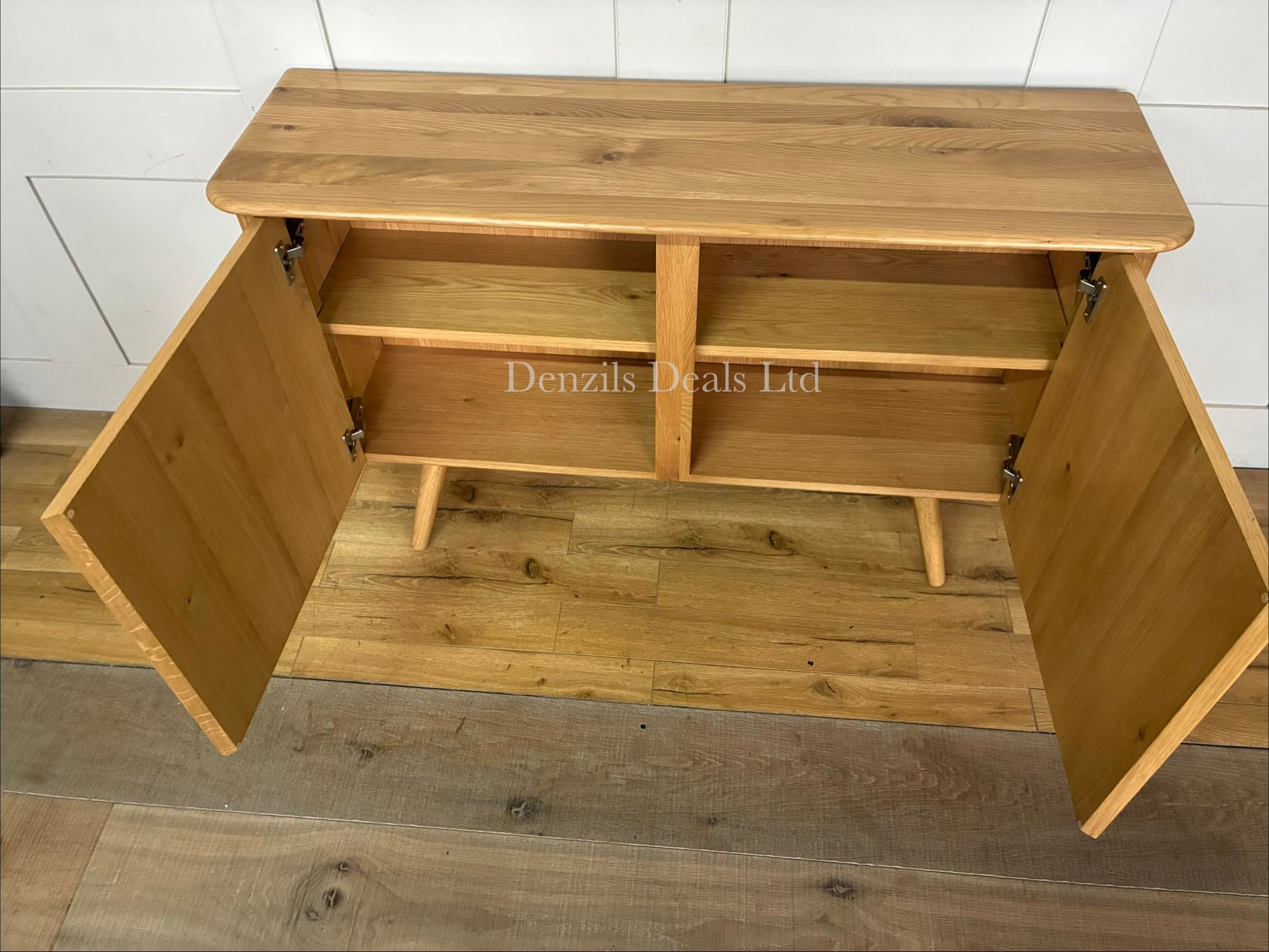 A contemporary two-door wooden sideboard from the John Lewis Greenwood range. The cabinet is crafted from light-toned solid oak and oak veneers, featuring a pale Bianco oiled finish that highlights the natural, linear wood grain. It has a clean, minimalist rectangular shape, flat-fronted double doors with subtle integrated handles, and sits flat against the floor.