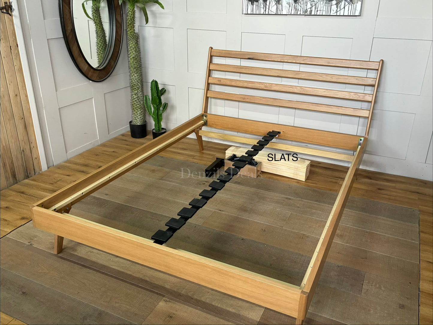 A king-size minimalist platform bed frame made of light natural oak wood. It features a high, slatted headboard with clean horizontal lines, tapered angled legs, and a sturdy sprung-slat base.