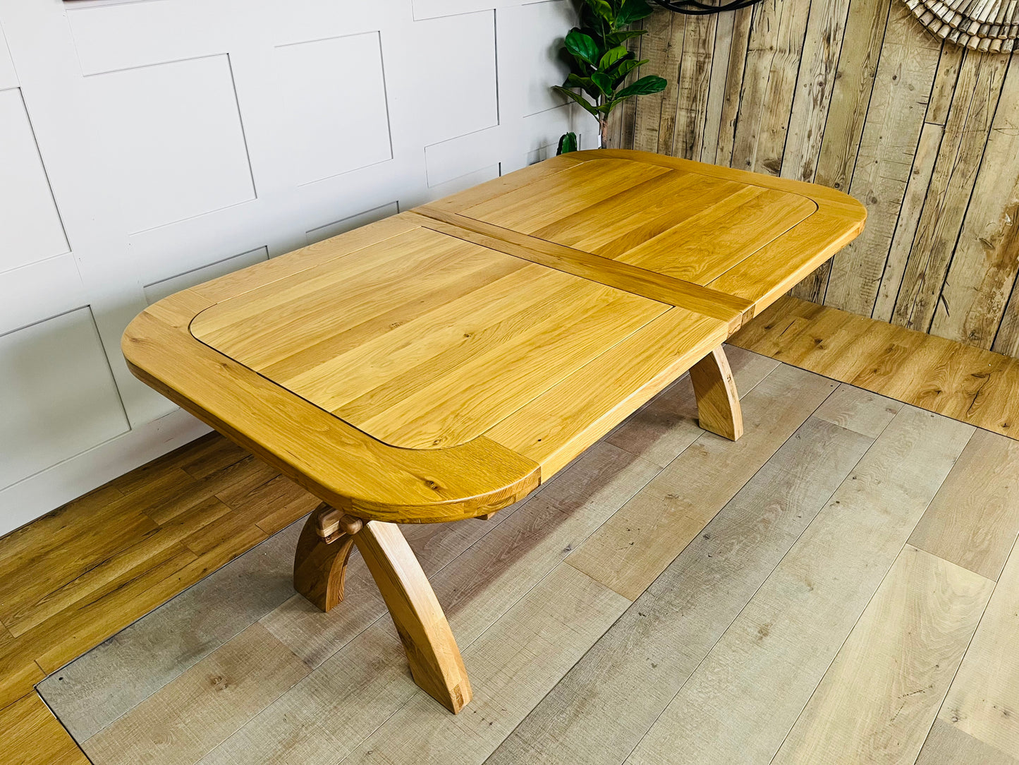 Large natural solid oak extendable dining table from Oak Furnitureland Hercules range featuring chunky cross-arched legs and chamfered beam.