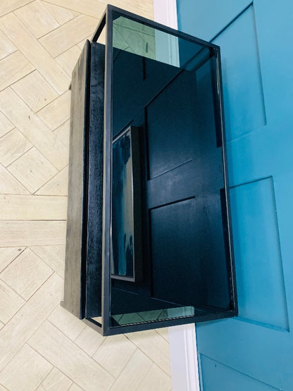 Modern Made.com Kilby TV stand featuring a solid mango wood base with a black stained finish. The unit includes a sleek single-drawer storage compartment and a smoked glass top, raised on slender, clean-lined metal legs