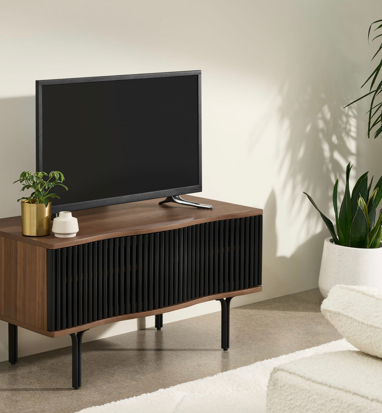 Made.com Zaragoza compact TV unit in organic walnut wood and charcoal black, featuring a contemporary slatted sliding front, subtle wavy edges, and slim metal legs