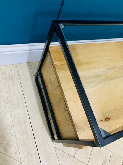A wide mid-century modern TV stand crafted from light golden mango wood. It features two sliding doors made of ribbed, fluted glass that partially reveal internal shelves. The unit sits on four slim, tapered wooden legs and has a clean, rectangular silhouette.