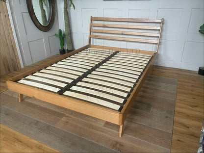 Mid-century modern king-size bed frame from the John Lewis X-Ray bedroom range, crafted from oak wood with a smooth Bianco Lacquer finish. The design features a slatted wood headboard with soft curves, sleek side panels, low-profile frame, and tapered wooden legs.