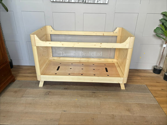 Minimalist SAZY kids cot bed crafted from natural solid spruce wood. The rectangular wooden frame holds durable, completely clear acrylic side panels. The structure sits on clean wooden legs, highlighting a light and airy nursery design suitable from birth up to 18 months.