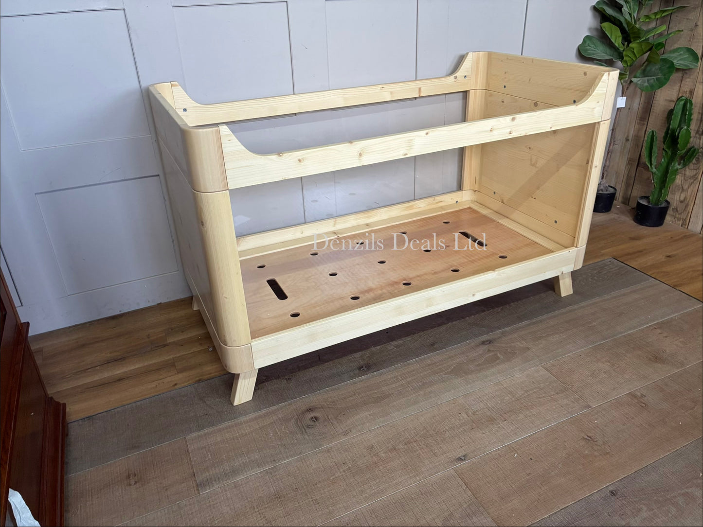 Minimalist SAZY kids cot bed crafted from natural solid spruce wood. The rectangular wooden frame holds durable, completely clear acrylic side panels. The structure sits on clean wooden legs, highlighting a light and airy nursery design suitable from birth up to 18 months.