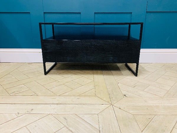 Modern Made.com Kilby TV stand featuring a solid mango wood base with a black stained finish. The unit includes a sleek single-drawer storage compartment and a smoked glass top, raised on slender, clean-lined metal legs