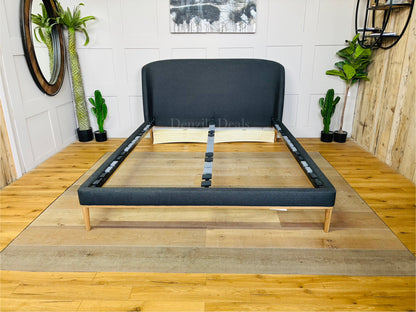 Modern bedroom setting featuring the John Lewis Show-Wood Upholstered King Bed in brushed tweed charcoal. The dark gray, textured fabric bed is styled with neutral bedding, highlighting its soft curves and minimalist wooden base