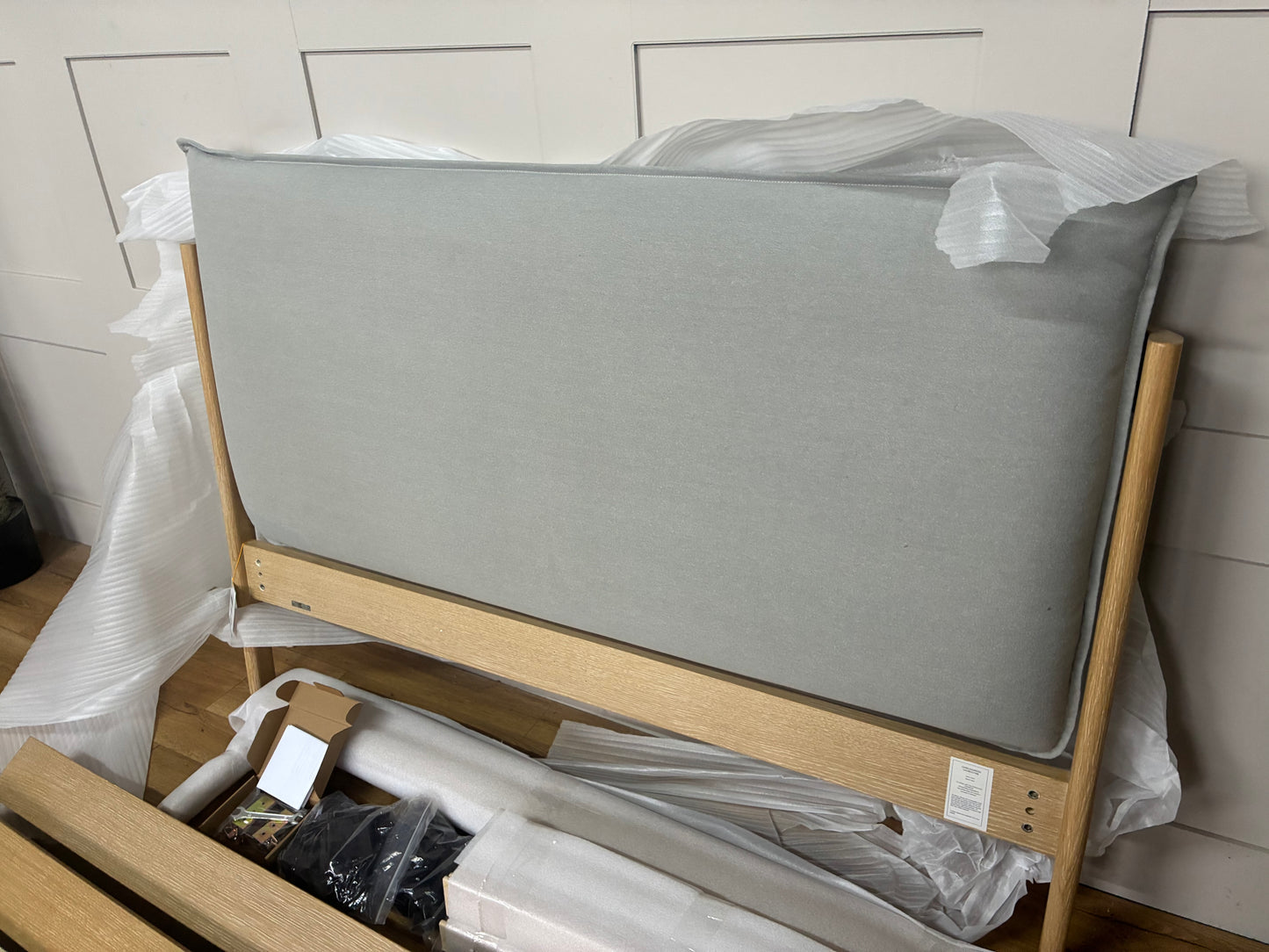 Modern double bed frame featuring a light natural oak wooden base and a soft, low-profile upholstered pillow headboard in grey fabric