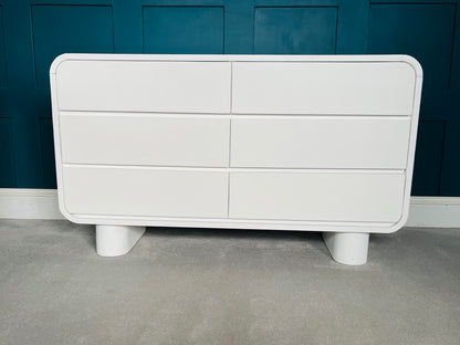 Modern low-slung bedroom dresser crafted from white-stained mango wood, featuring six spacious drawers with integrated grooved handles, soft curved corners, and two thick cylindrical block feet