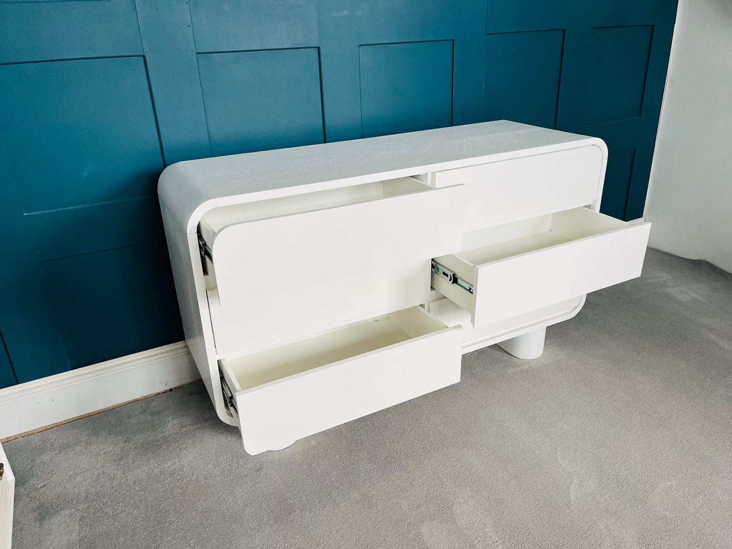 Modern low-slung white lacquered dresser with rounded edges and cylindrical block feet.