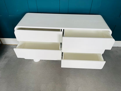 Modern low-slung white lacquered dresser with rounded edges and cylindrical block feet.
