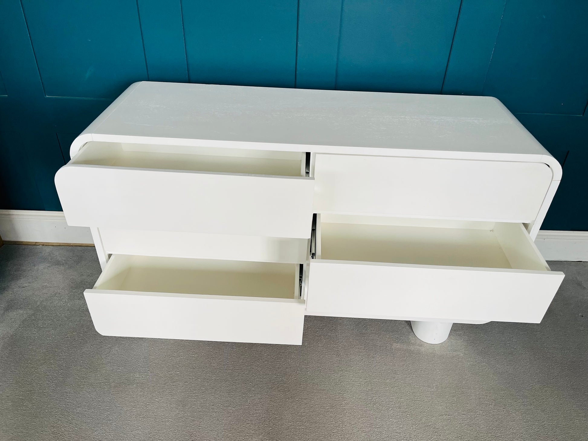 Modern low-slung white lacquered dresser with rounded edges and cylindrical block feet.
